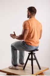 Sitting pose orange thsirt light blue jeans of bodybuilder Harold